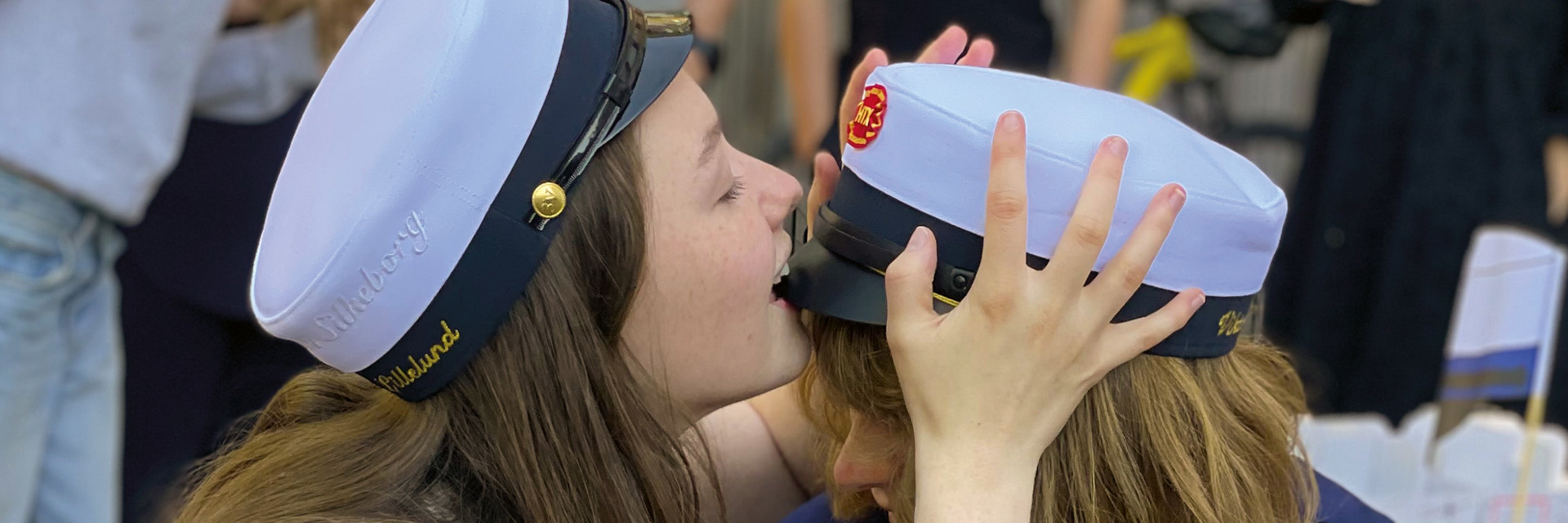 To HTX piger med studenterhuer - den ene pige bider i skyggen på den andens hue