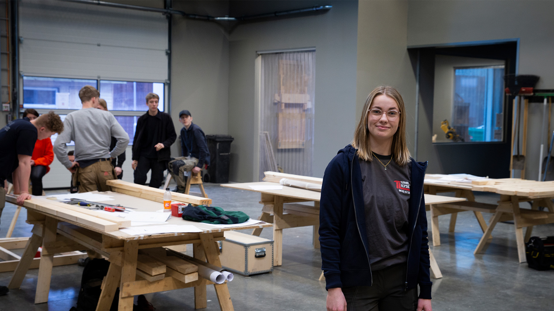 Kvindelig tømrer står i front, mens gruppe af mandlige tømrere står i baggrunden