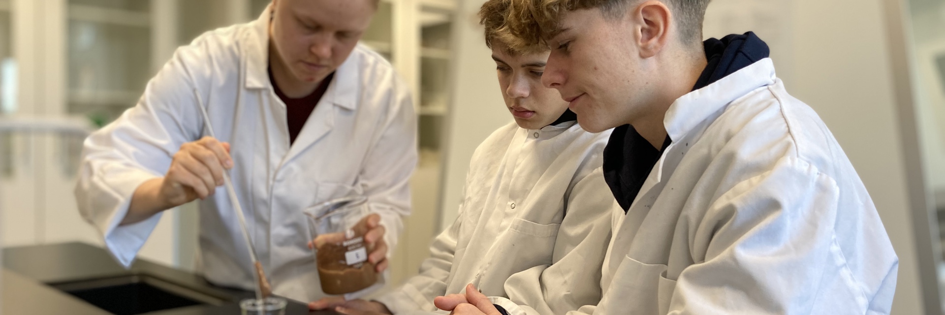 Tre HTX elever i hvide kitler laver forsøg i laboratorium