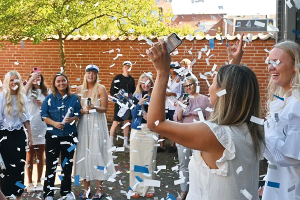Pige kommer ud fra sidste eksamen og fejres af venner og familie med konfetti, før huen sættes på