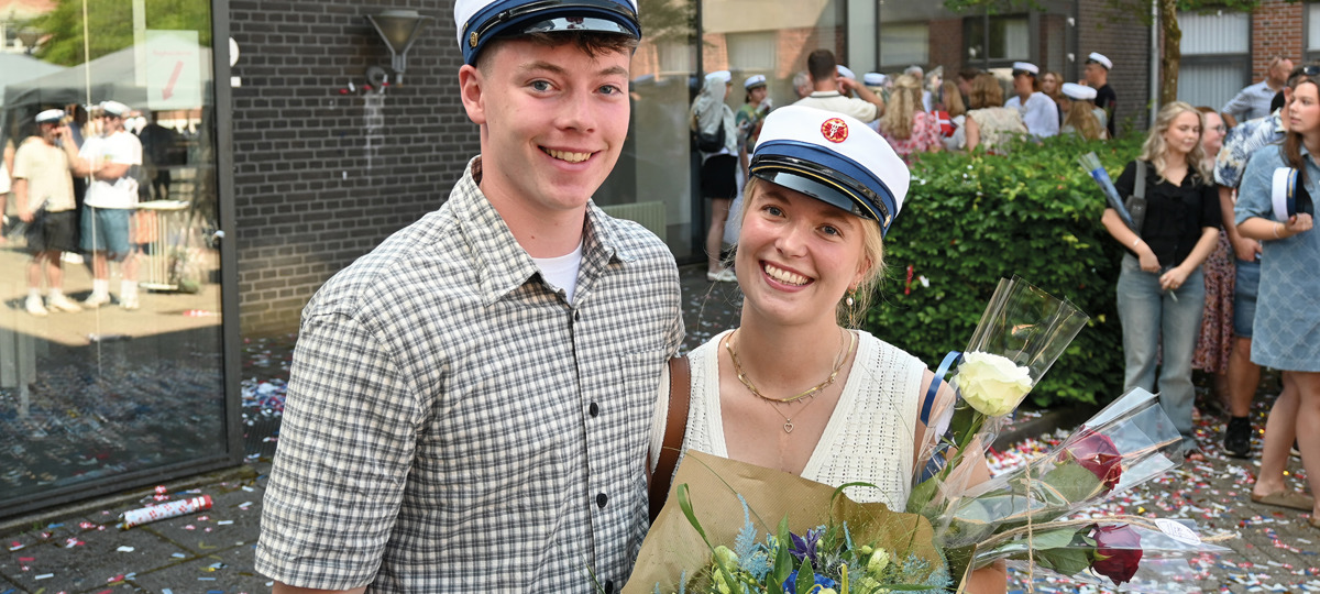 To smilende HHX studenter med hue på