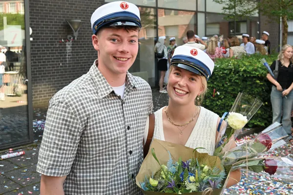 To smilende HHX studenter med hue på
